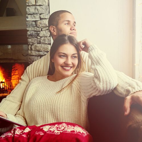 a couple cuddling in front of a stove fire